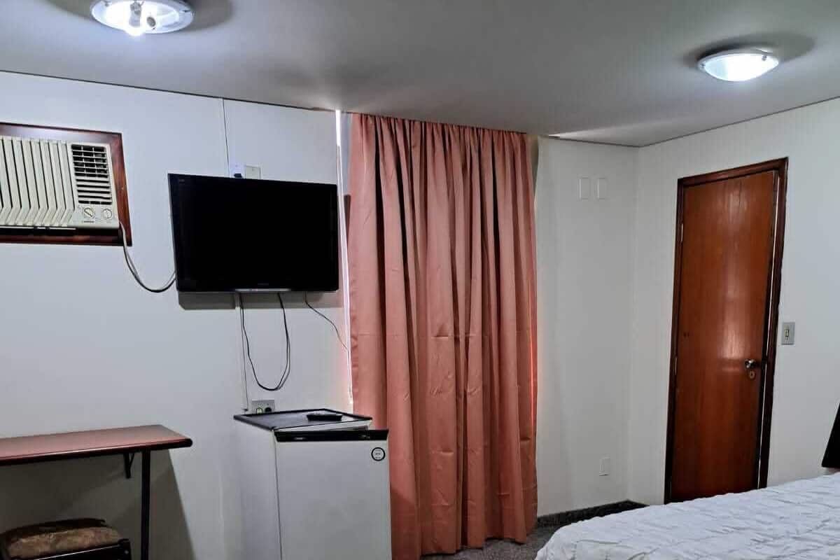 A hotel room with two beds, a TV, a desk, a small table, a chair, a door, and a window with curtains.