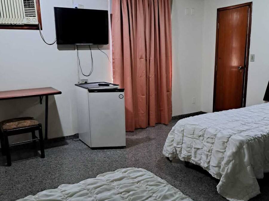 Hotellihuone, jossa on kaksi sänkyä, televisio, työpöytä, pieni pöytä, tuoli, ovi ja ikkuna, jossa on verhot.
