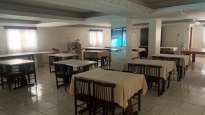 A dining area with multiple tables and chairs, a tiled floor, and a large window with curtains. - Avalon (Goiânia)