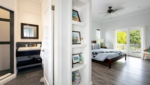 A bedroom with a bed, a nightstand, a window with a view of greenery, and a balcony. - Salty Dolphin 4 Bedroom Home (Governor's Harbour)