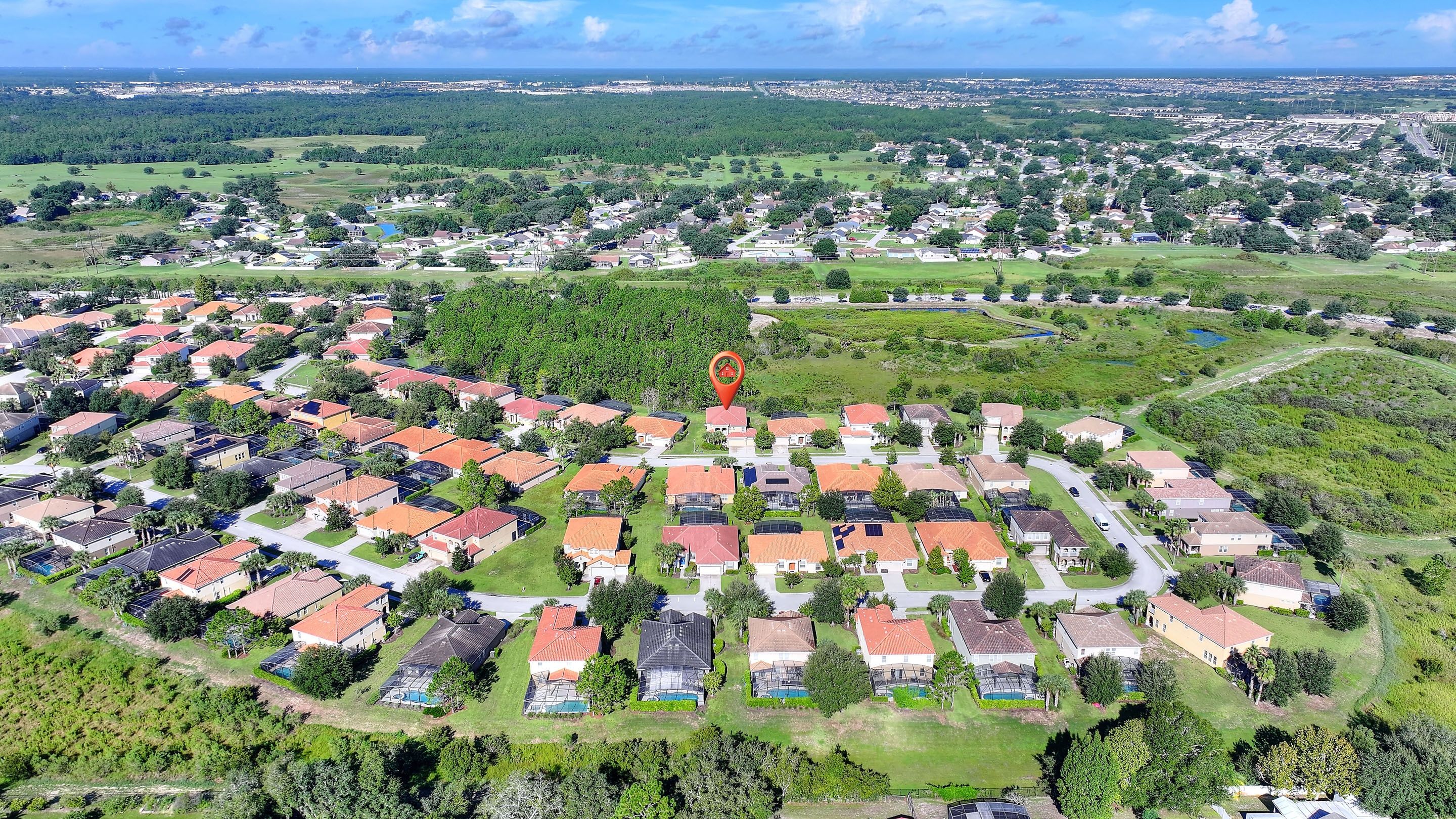 A residential area with houses arranged in a grid pattern, surrounded by greenery and a distant view of a cityscape.