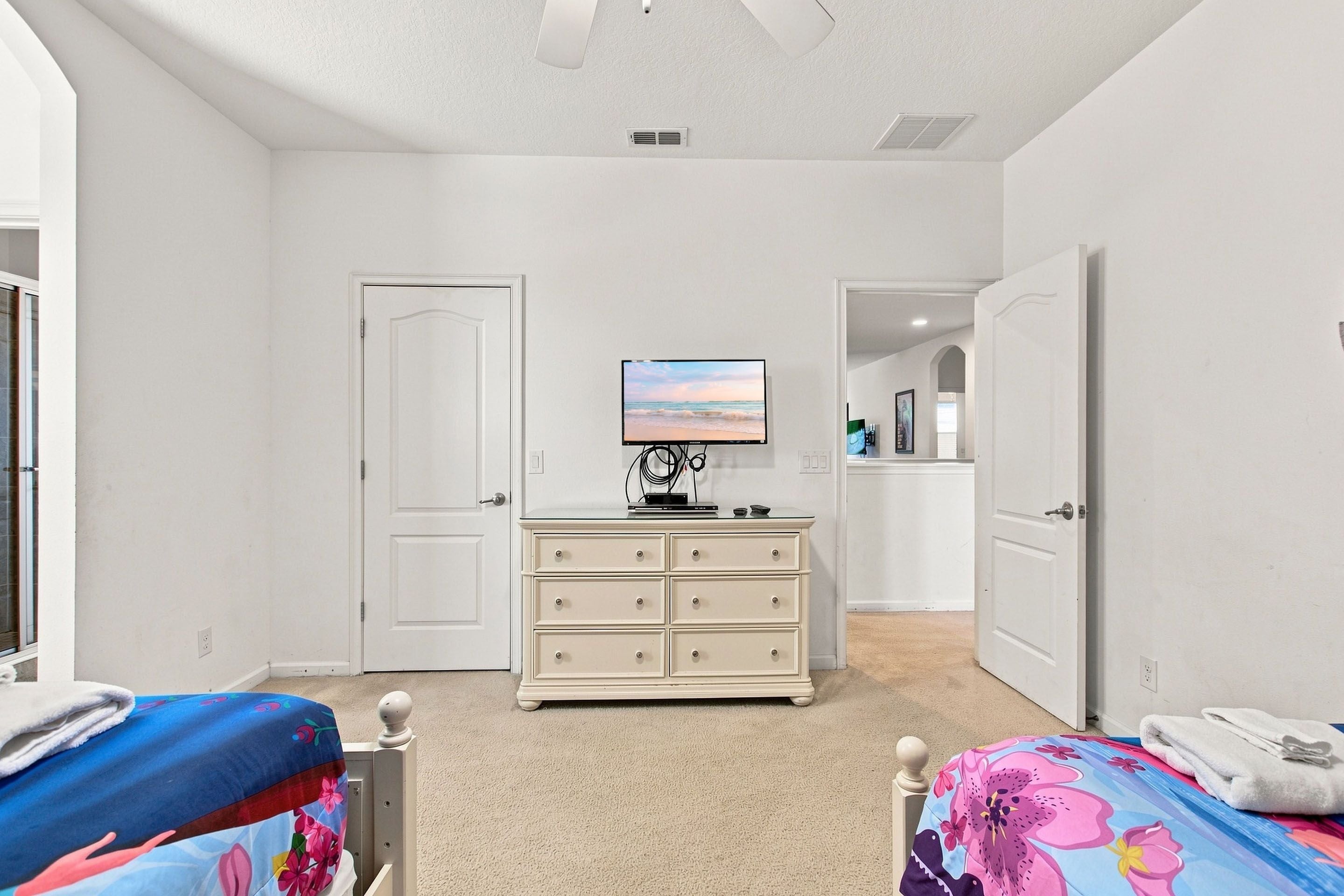 A bedroom with a bed, a dresser, a television, and a door leading to another room.