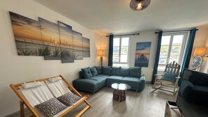 A living room with a sectional sofa, a wooden-framed lounge chair, a round coffee table, and a television.