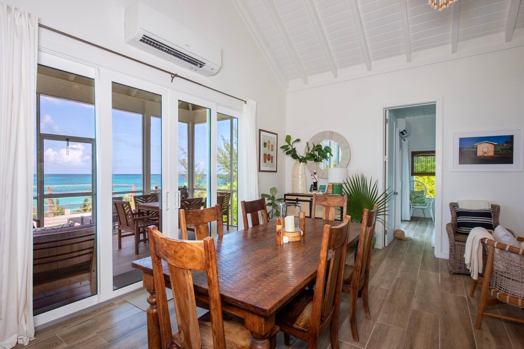 A spacious dining area with a large wooden table and chairs, large windows with ocean views, and a ceiling fan.