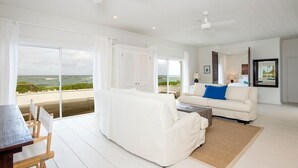Ett rymligt vardagsrum med en vit soffa, ett matbord med stolar och utsikt över havet genom stora fönster.
