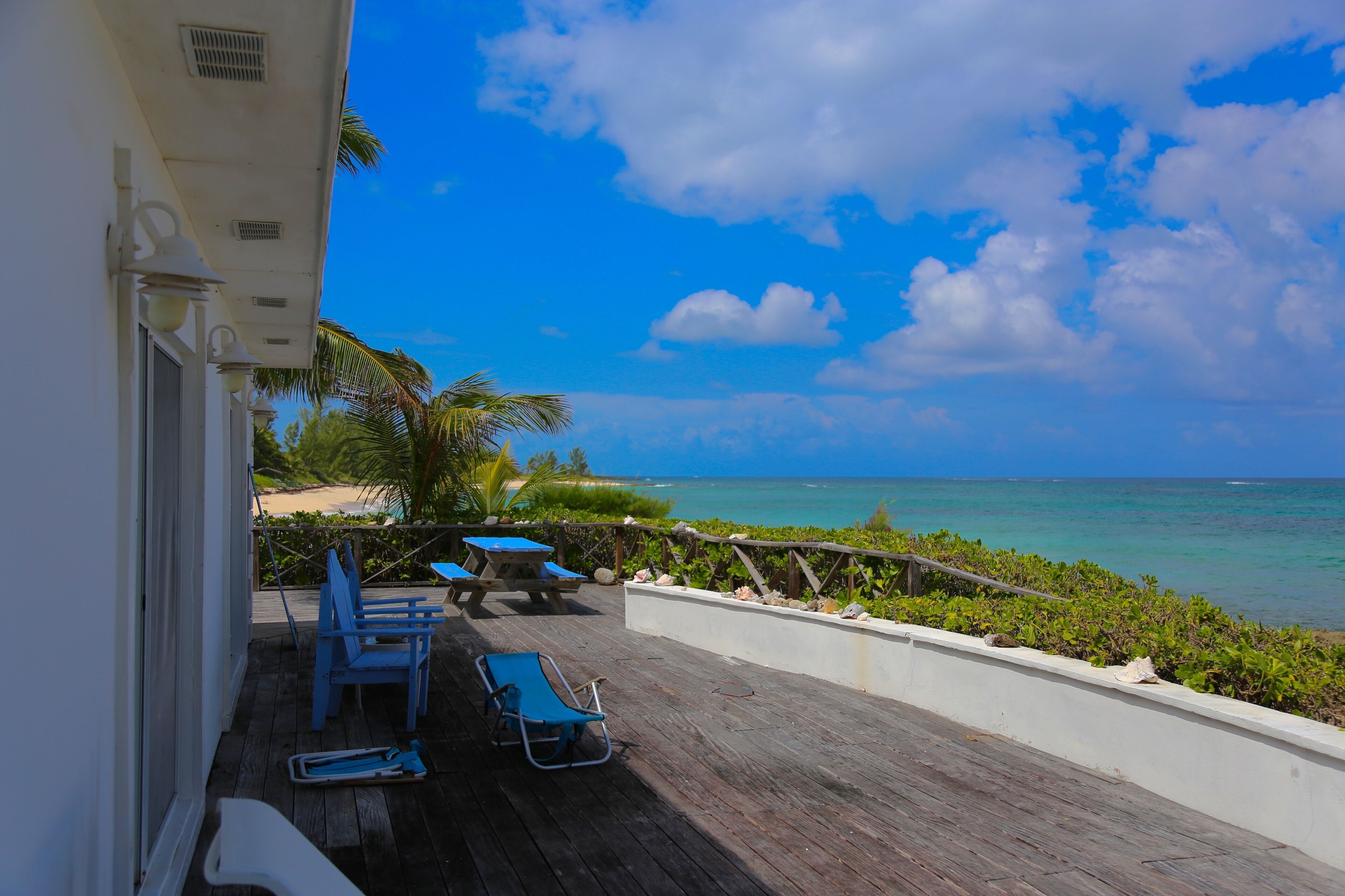 Eine Holzterrasse mit blauen Stühlen und einem Tisch mit Blick auf Strand und Meer.