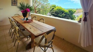 Un comedor con mesa de madera y sillas de mimbre, una planta en maceta y vistas al exterior.