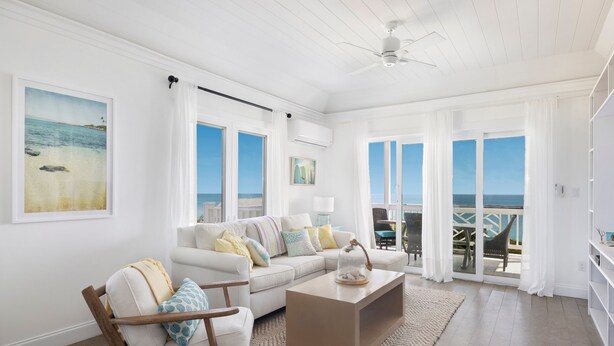 A spacious living room with a white sofa, a wooden chair, a coffee table, and a view of the ocean through large windows. - Buttonwood Reserve by Eleuthera Vacation Rentals (James Cistern)