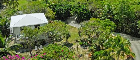 Un edificio blanco con techo triangular rodeado de abundante vegetación y un pequeño arroyo.