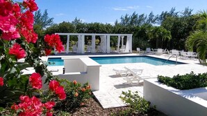 Ein Poolbereich mit weißen Liegestühlen, einer weißen Pergola und üppiger Bepflanzung.