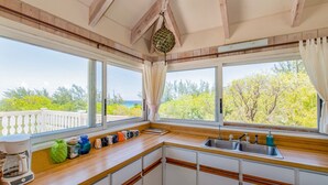 Eine Küche mit Holzarbeitsplatten, weißen Schränken, einer Kaffeemaschine und Meerblick durch große Fenster.