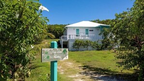 Edificio blanco con balcón, rodeado de exuberante vegetación y un letrero que dice 'Key Lime Cottage'.