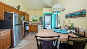 Una cocina con armarios de madera, un refrigerador de acero inoxidable, una mesa de comedor con sillas y una lámpara colgante.