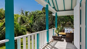 A wooden deck with a white railing, a bench, and a table with a plant. - Orchid Cottage 2 Bedroom Cottage (Governor's Harbour)