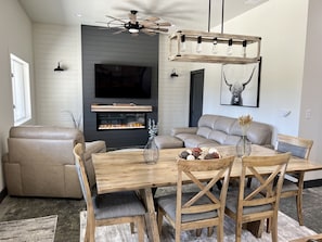Een moderne woonkamer met een open haard, een houten eettafel en een bank.