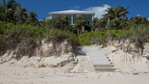 Une propriété située en bord de mer, avec un escalier menant à une maison entourée de palmiers et de végétation.
