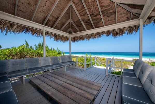 A wooden deck with benches and a thatched roof overlooking a beach.