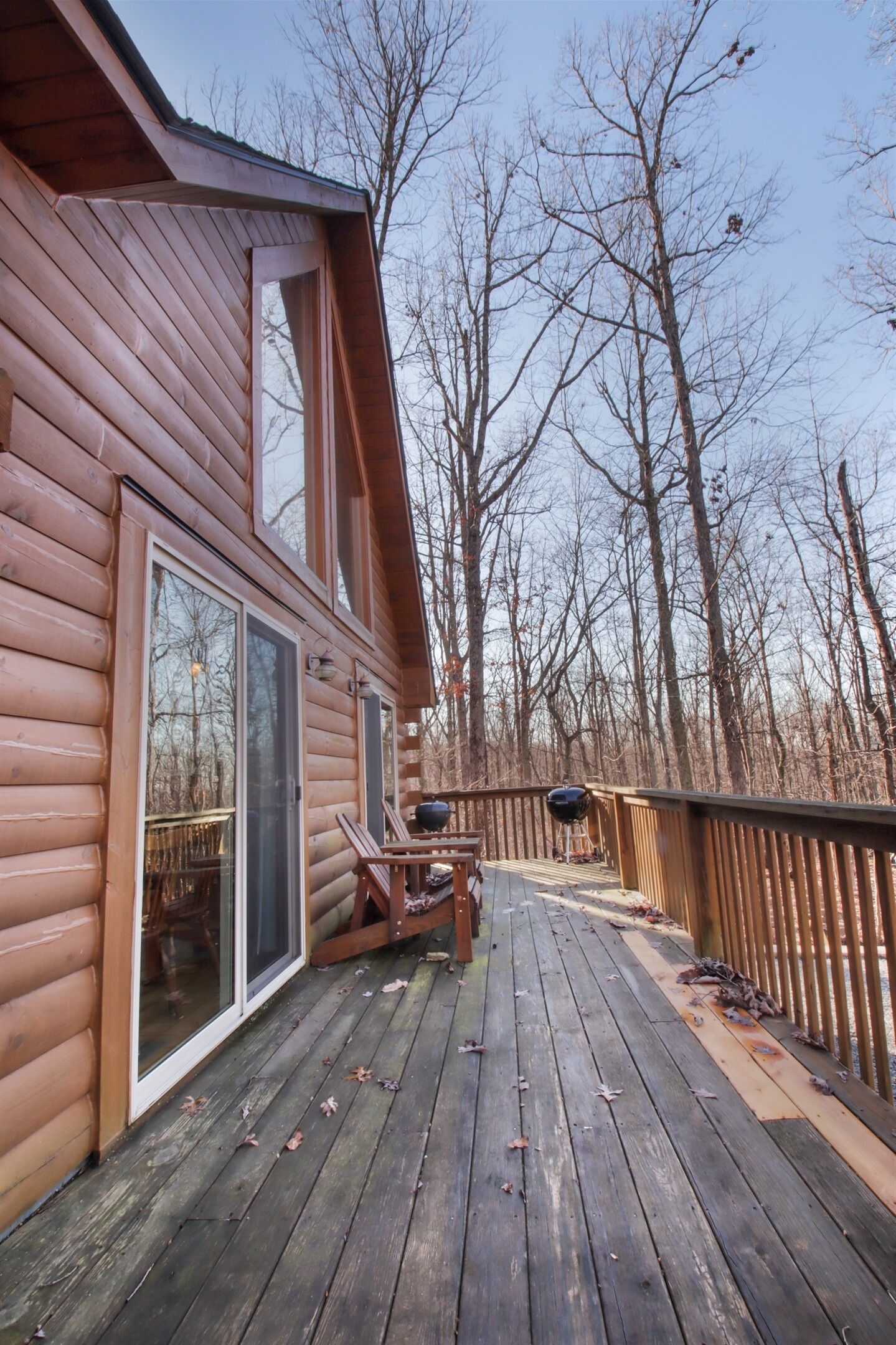 A wooden cabin with a deck, large windows, and a view of leafless trees.