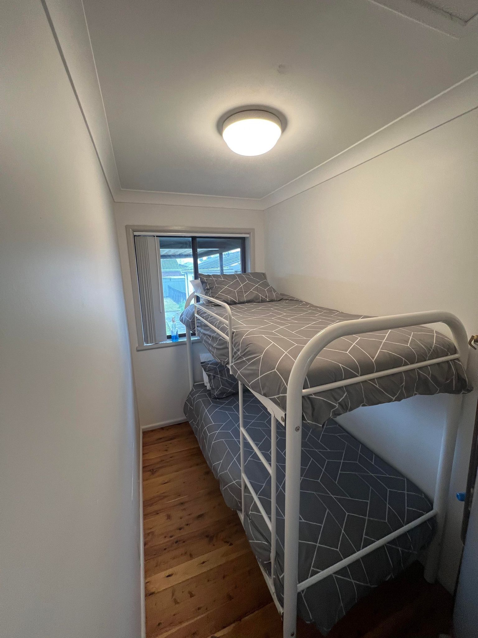 Une chambre avec un lit superposé, une fenêtre, un plancher en bois et un luminaire au plafond.