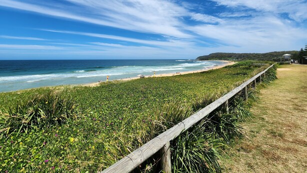 Paisaje costero con valla de madera, playa y océano.