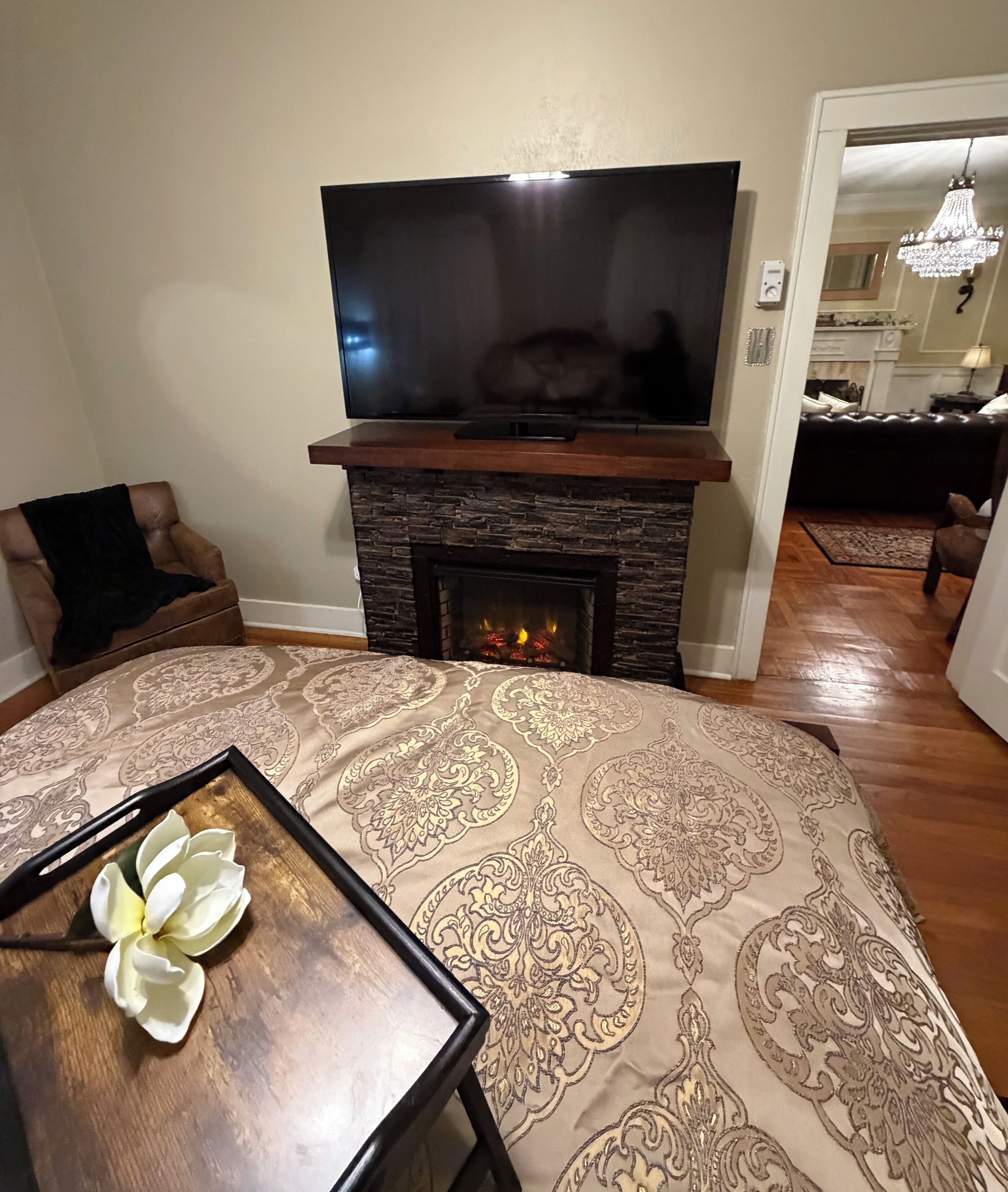 A living room with a fireplace, a television, a patterned rug, and a table with a flower.