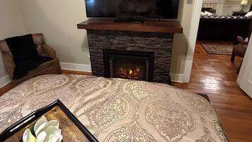 A living room with a fireplace, a television, a patterned rug, and a table with a flower.