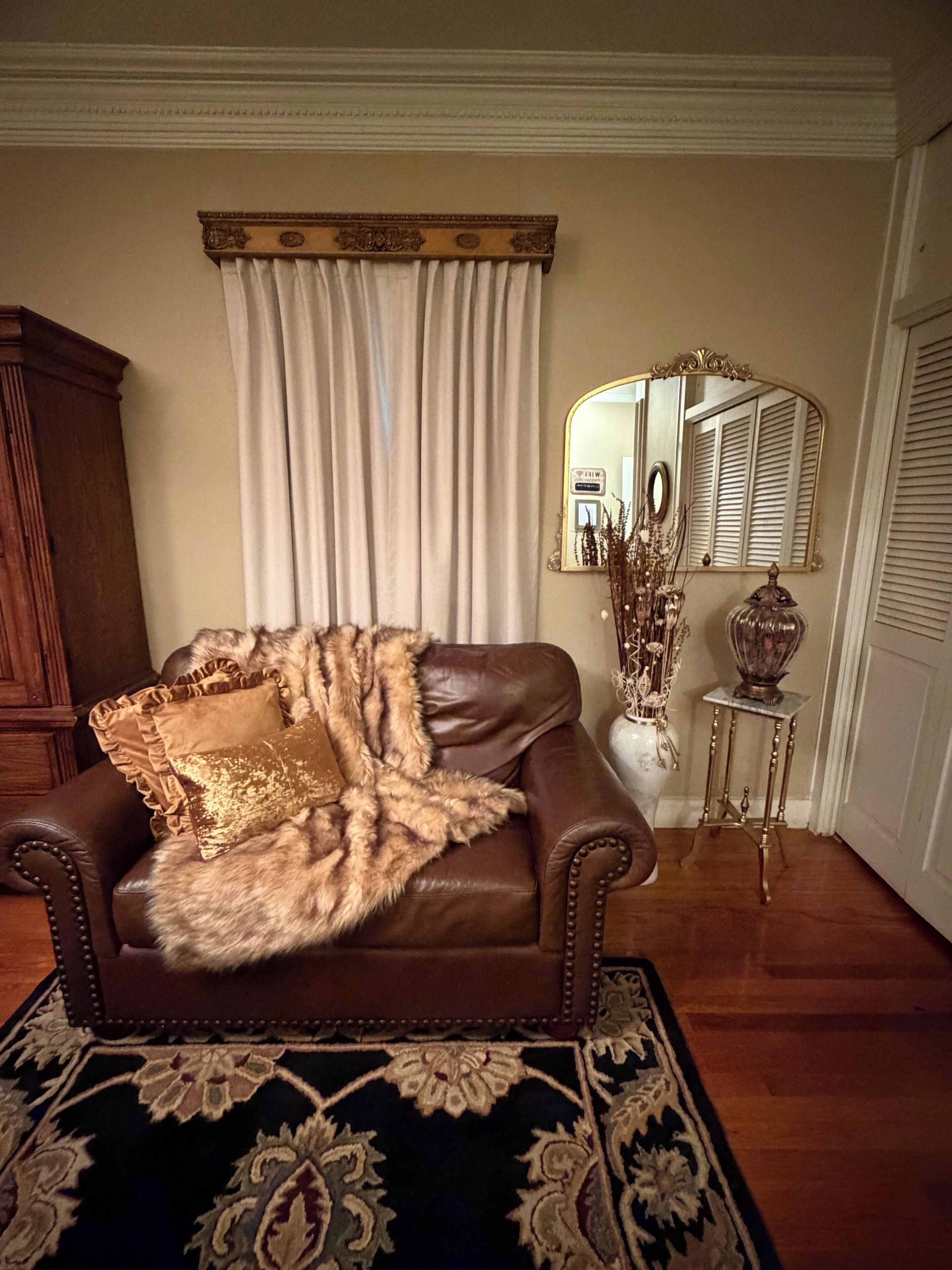 A brown leather armchair with a fur throw, a mirror, a vase with dried plants, and a wooden cabinet.
