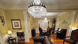 Amplia sala de estar con un sofá de cuero grande, un candelabro elegante, un comedor y un piano.