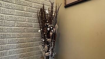 Un jarrón blanco con un arreglo floral frente a una pared de ladrillo con una obra de arte de una mariposa en marco.
