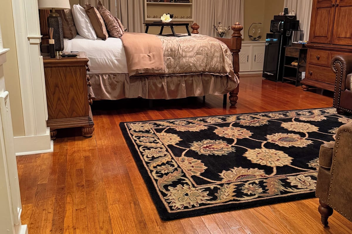A bedroom with a large bed, a wooden dresser, a nightstand, a chandelier, and a patterned rug.