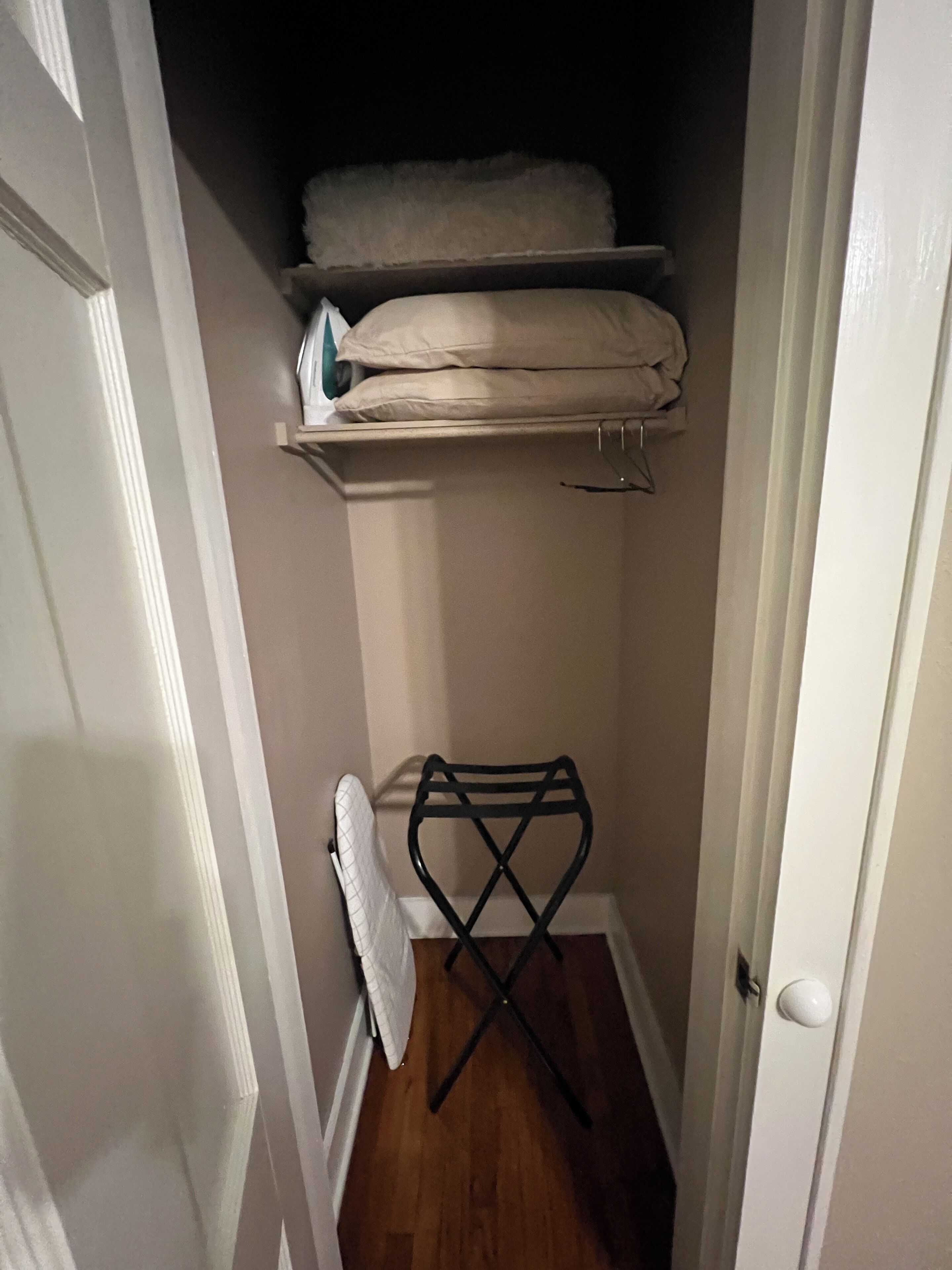 A narrow hallway with a wooden floor, a black ironing board, and a white door.