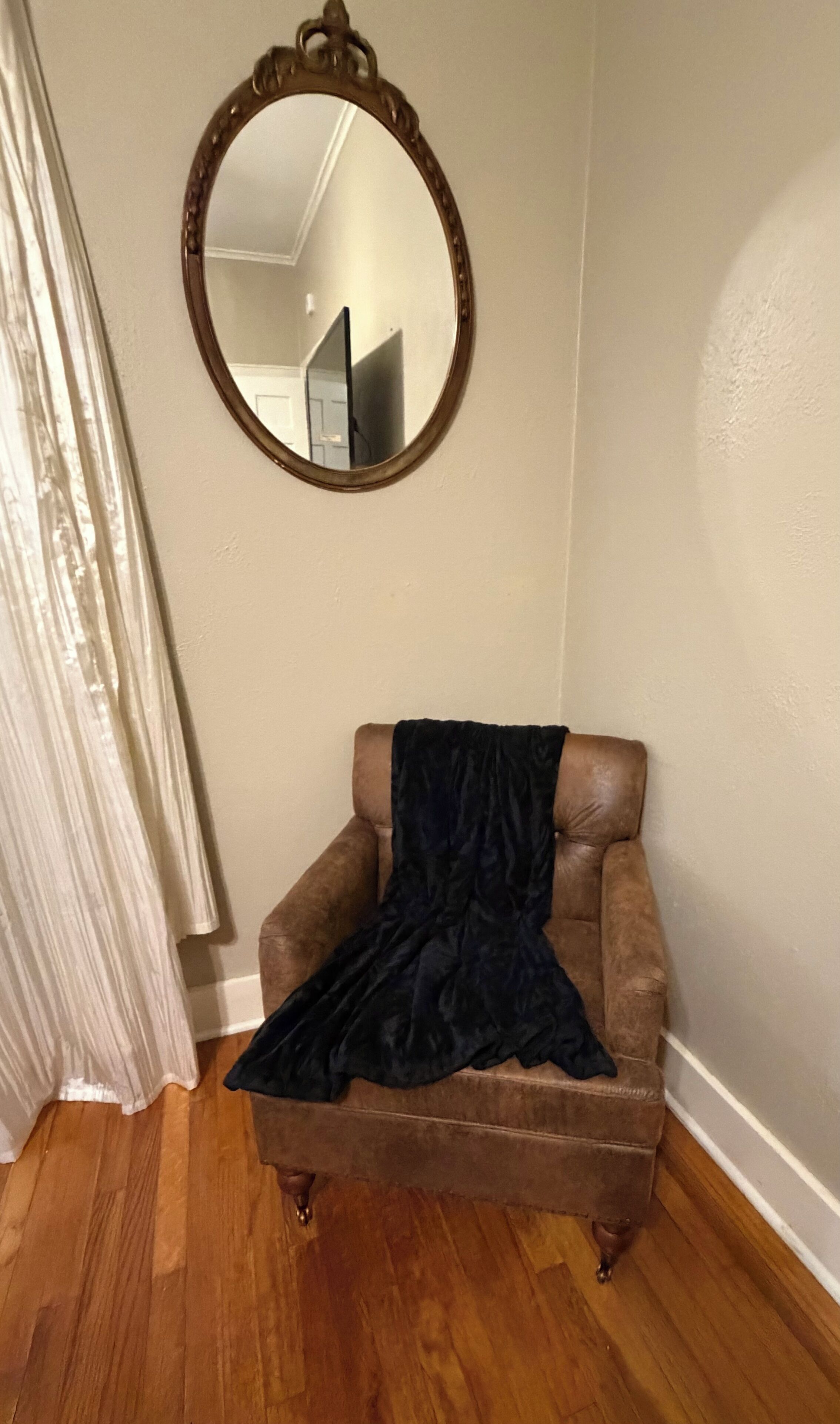 Une pièce avec un fauteuil marron, un miroir au mur et un plancher en bois.
