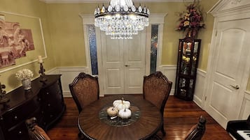 Comedor con una mesa redonda, sillas ornamentadas, una araña y un espejo grande.