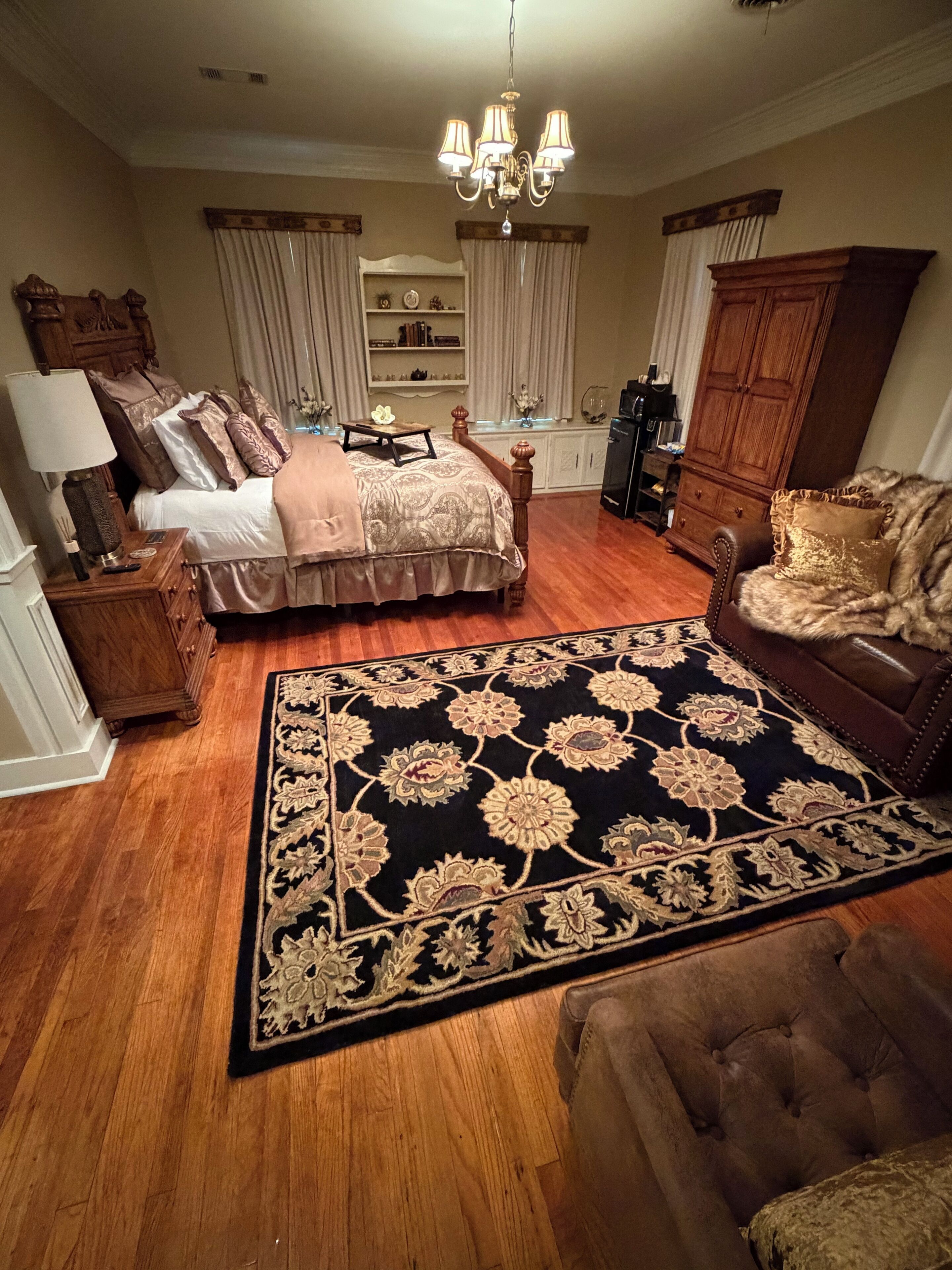 A bedroom with a large bed, a chest of drawers, a nightstand, a dresser, a chandelier, and a large rug.