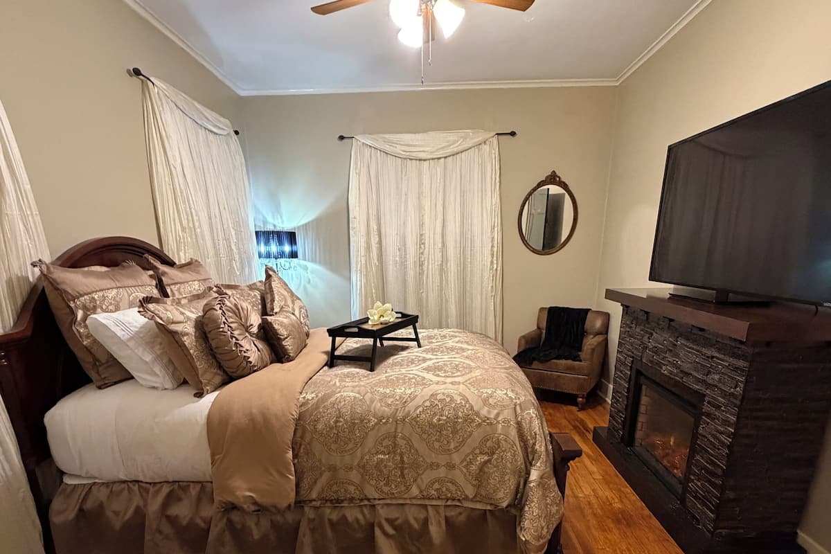 A bedroom with a bed, a ceiling fan, a fireplace, and a television.
