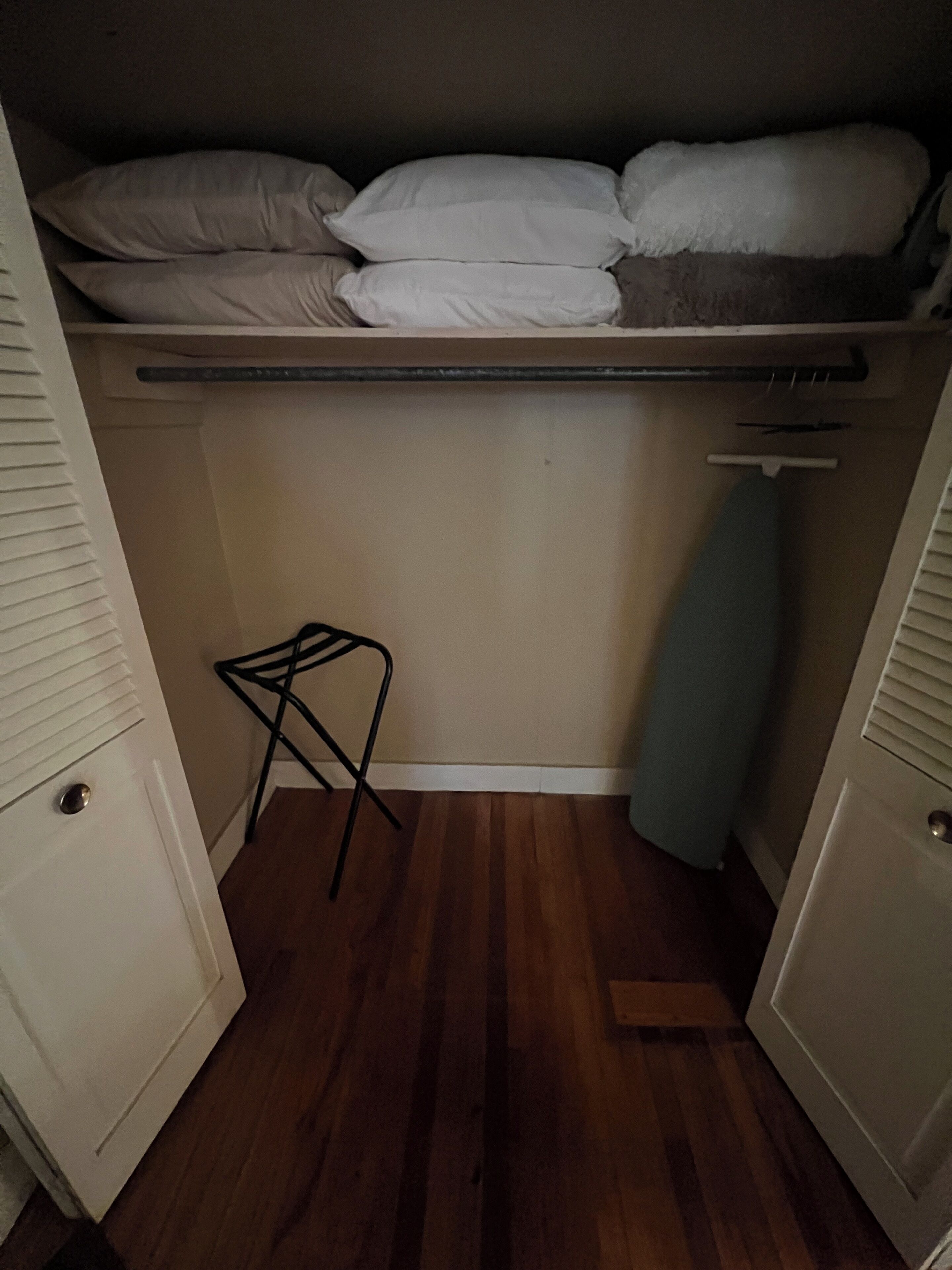 A bedroom with a bed, a small stool, and a hanging laundry rack.