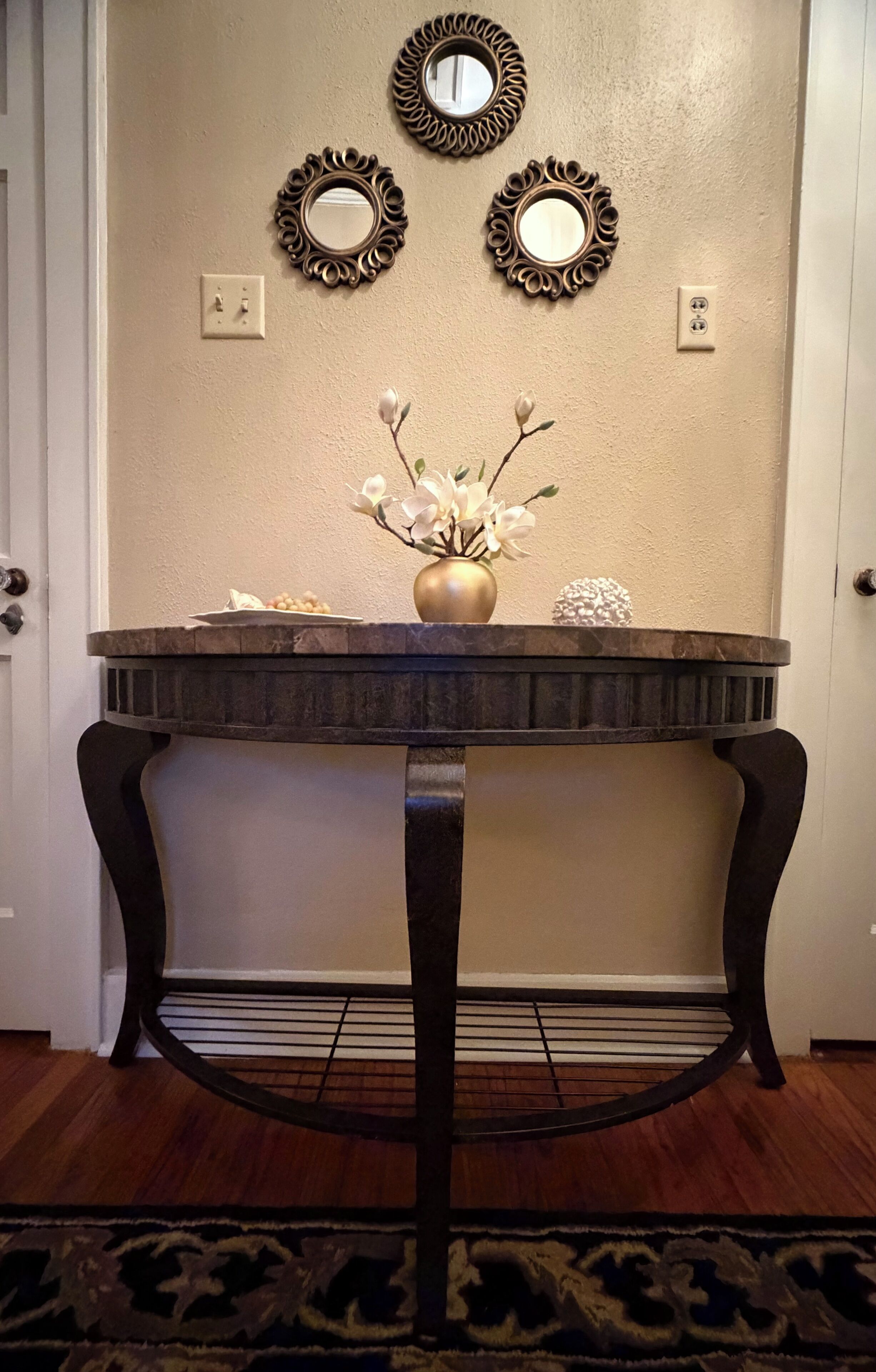 A round table with a vase of flowers, three wall mirrors, and a textured wall.