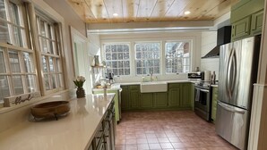 Een keuken met houten plafond, groene kasten, een roestvrijstalen koelkast en een groot raam.