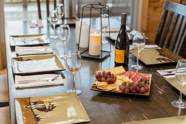 A dining table set with plates, cutlery, glasses, a candle, a bottle of wine, and a platter of grapes and cheese.
