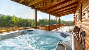 Een houten chalet met een hottub op een terras, omringd door bomen.