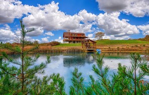 A large wooden house with a deck and a pond in front.