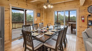 Een houten chalet met een eethoek, ingericht voor een maaltijd, met een lange tafel, stoelen en een kroonluchter.