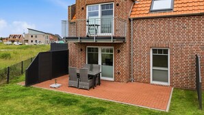 Une maison à deux étages, construite en briques, dotée d’un balcon, d’une antenne parabolique et d’une terrasse dallée aménagée avec du mobilier d’extérieur.