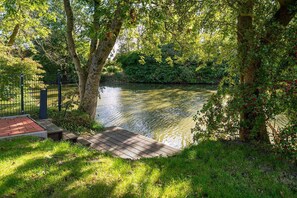 Ein Flussuferweg mit Holzdeck, umgeben von Bäumen und Grünpflanzen.