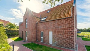 Un bâtiment en briques de deux étages, avec un toit recouvert de tuiles rouges, une petite fenêtre et une allée pavée.