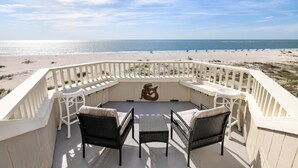 A balcony with wicker furniture overlooking a beach.