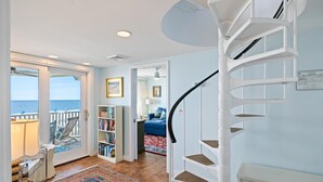 A spiral staircase, a balcony with a view of the sea, and a living area with a sofa and bookshelves.