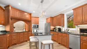 Una cocina moderna con armarios de madera, una isla central con taburetes, electrodomésticos de acero inoxidable y un ventanal grande.