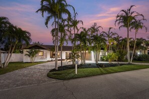 A modern house with a paved driveway, surrounded by palm trees and a well-maintained lawn.