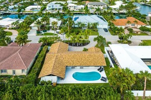 A residential area with a large house featuring a swimming pool, surrounded by palm trees and other houses.
